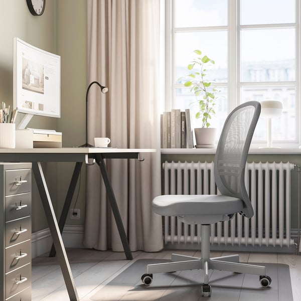 Modern home office with FLINTAN gray mesh chair, white desk, computer, books, plant, and radiator.