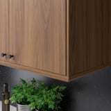 Wooden kitchen cabinet with dark knobs and grey backsplash. Herbs and bottle on counter.