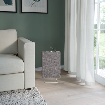 Small, modern gray air purifier beside white couch.