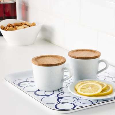 Two white mugs with bamboo lids on a tray with lemon slices, demonstrating their use as mug covers.