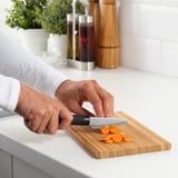 Person prepares vegetables using a FÖRSLAG knife on a wooden cutting board.