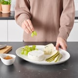 Person setting grapes on plate with cheeses and fruit.