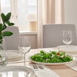Table set with white plates, cutlery, and wine glasses; fresh salad on a plate, chairs around.