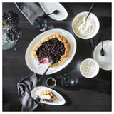 Dark table set with white FRÖJDEFULL dinnerware, including dessert and berry tart.