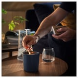 Person lighting blue scented candle on wooden table next to empty glass.