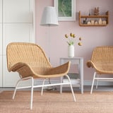 Two wicker armchairs, white legs, rug, side table with flowers, lamp, shelf with decor.