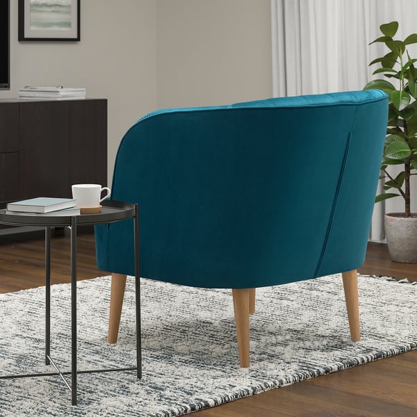 Teal FULLÖSA armchair with wooden legs, on striped rug beside side table with mug and books.