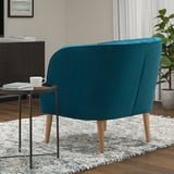 Teal FULLÖSA armchair with wooden legs, on striped rug beside side table with mug and books.