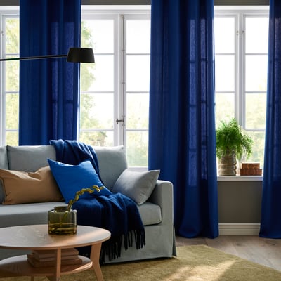Modern living room with large GINSTMOTT dark blue curtains; light blue sofa, cozy throw, and natural coffee table.