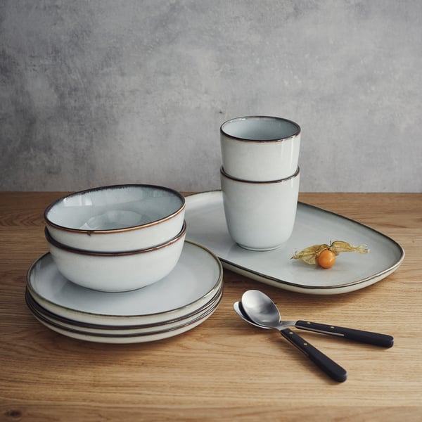 GLADELIG tableware set in sandy glaze, stoneware, includes bowls, plates, cups, spoon, knife. Stacked compactly. Decorative, classic shapes.