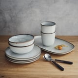 GLADELIG tableware set in sandy glaze, stoneware, includes bowls, plates, cups, spoon, knife. Stacked compactly. Decorative, classic shapes.