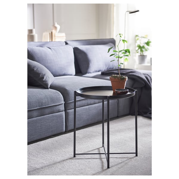 Small black metal side table with a round white tray top, holding a potted plant next to a gray sofa.