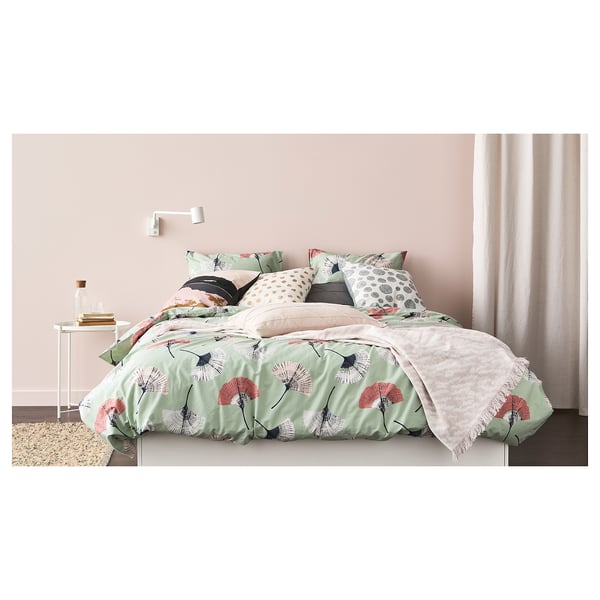 Bed with green floral comforter, beige curtains, bedside books, and wall light.