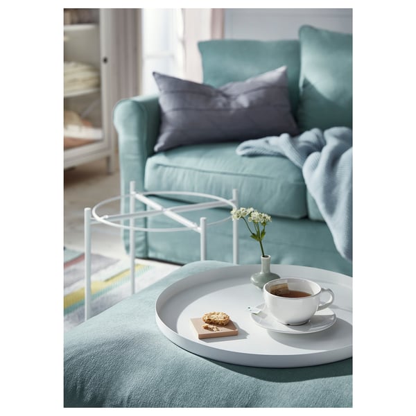 Modern living room with turquoise sofa, white side table holding coffee cup, biscuit, and small vase with white flowers.