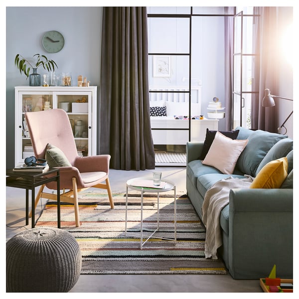 Bright living room with a cozy chair, colorful couch, modern coffee table, and stylish rug. Large windows let in natural light.