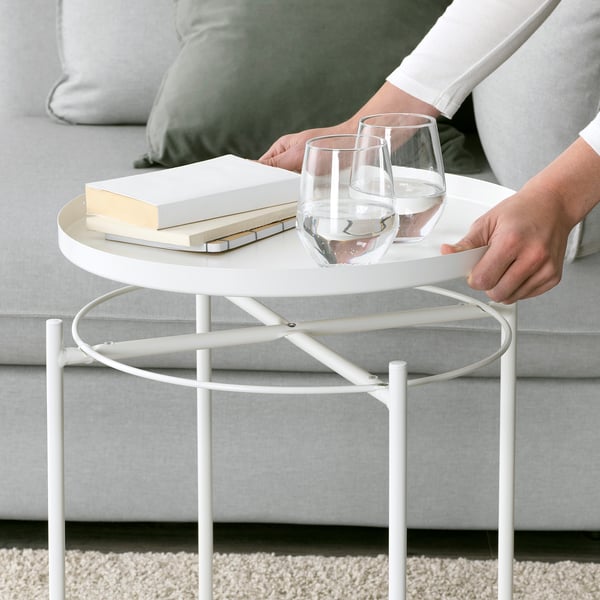 Person places wine glasses on GLADOM side table. Modern, white, circular tray top over metallic base. Simple and convenient design for serving.