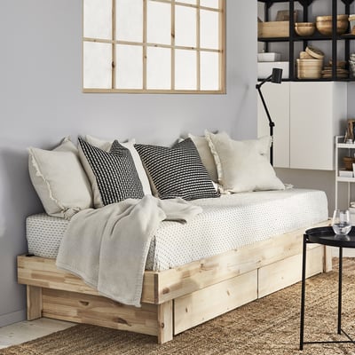 GLAMBERGET wood bed with white bedding and pillows. Black side table with wine glass. White wall decor.