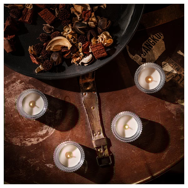 Four lit candles in silver holders surround a large black bowl filled with dried potpourri. The setup rests on a rustic, wooden surface.