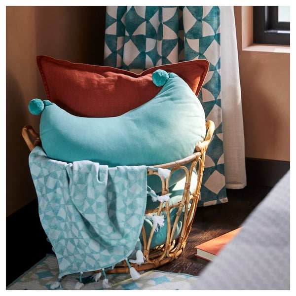 Wicker basket holding two colorful pillows, teal and orange, with pom-poms.