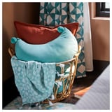 Wicker basket holding two colorful pillows, teal and orange, with pom-poms.