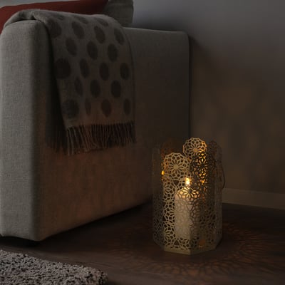 GOKVÄLLÅ lantern on floor beside couch; small, octagonal, lit, metallic glow.