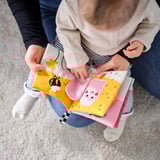 Adult and child reading a soft, interactive playbook with fabric figures, textures, and sensors.