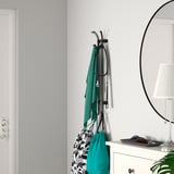 Gray wall-mount coat rack with green towels and bags, next to white dresser and round mirror.