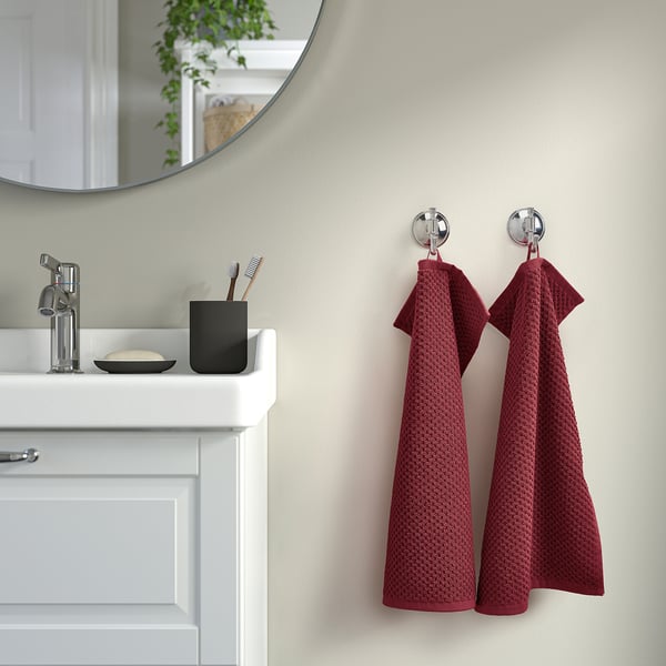 Red GULVIAL towels hang on wall hooks next to white sink and black toothbrush holder.