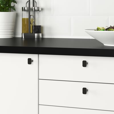 Two sleek black HACKÅS knobs, one t-shaped, one rectangular, smooth and modern.