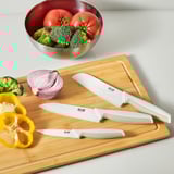 A set of three knives on a wooden cutting board with fresh vegetables. Ready for slicing, chopping, and dicing tasks in the kitchen.