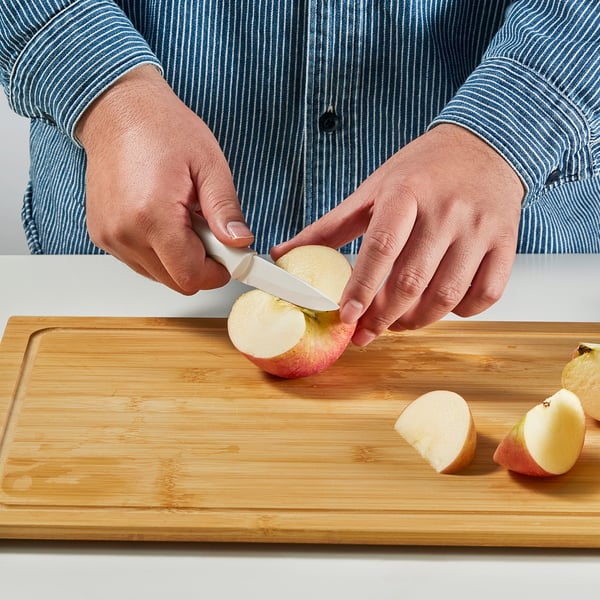 Person slicing apple on wooden cutting board using a ceramic knife.