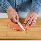Person slicing food with a ceramic knife on a wooden cutting board.