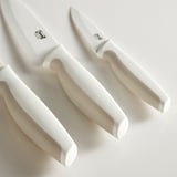 Three ceramic knives with white handles in a stand, showcasing sharp, well-crafted blades and ergonomic grips.