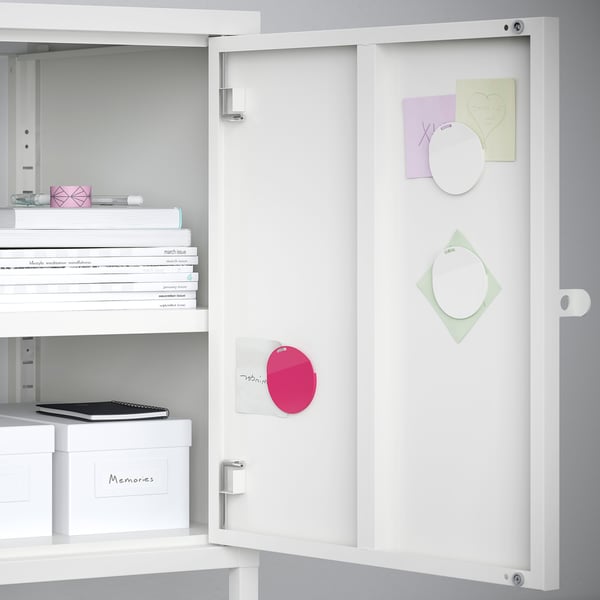 White cabinet door with magnets and notes. Shelves with books and boxes inside.