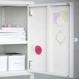 White cabinet door with magnets and notes. Shelves with books and boxes inside.