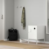 White HÄLLAN cabinet beside door, smaller than nearby backpack, locks.