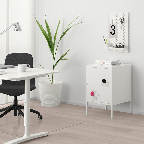Small white HÄLLAN cabinet with magnets, next to a desk and plant.