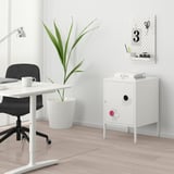 Small white HÄLLAN cabinet with magnets, next to a desk and plant.