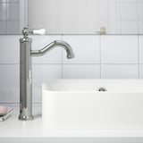 Modern chrome faucet with white ceramic lever and aerator, mounted on white bathroom countertop.