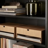 Black bookshelf with wooden drawers for storage, featuring books, decorative items.