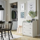 Modern room with white HAUGA chest, black chairs, plant, and art.