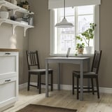 Small HAUGA table & chairs, light wood, black chairs near window with shelves.
