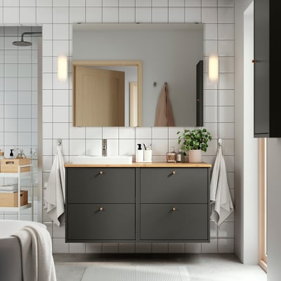 Modern bathroom with dark grey vanity, bamboo counter, white basin. Wall-mounted, gold handles. Mirror with lights, towels, plant.