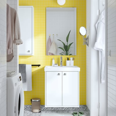 Yellow tiled bath. White vanity, plant. Machine left, towels hanging.