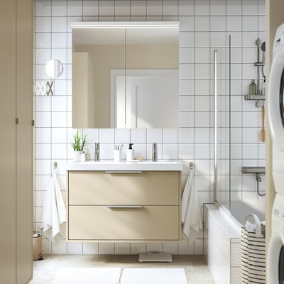 Modern bathroom with HAVBÄCK beige vanity. Large mirrored cabinet, double sink, sleek design. Towels and toiletries neatly arranged.