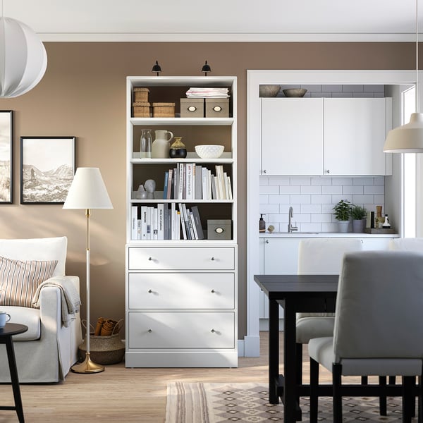 Modern living area with HAVSTA storage unit. White drawers and shelves between couch and kitchen. Decorated, stylish rug.