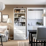 Modern living area with HAVSTA storage unit. White drawers and shelves between couch and kitchen. Decorated, stylish rug.