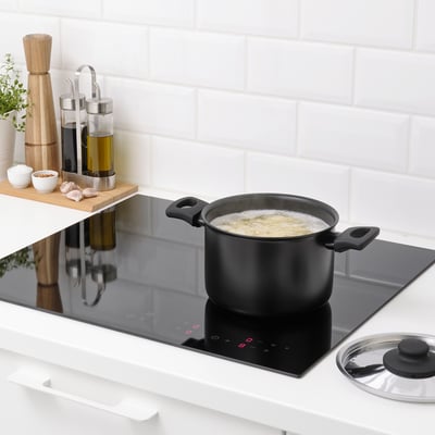 Kitchen scene: black saucepan with steam vents heats food on stove, wooden accessories nearby.