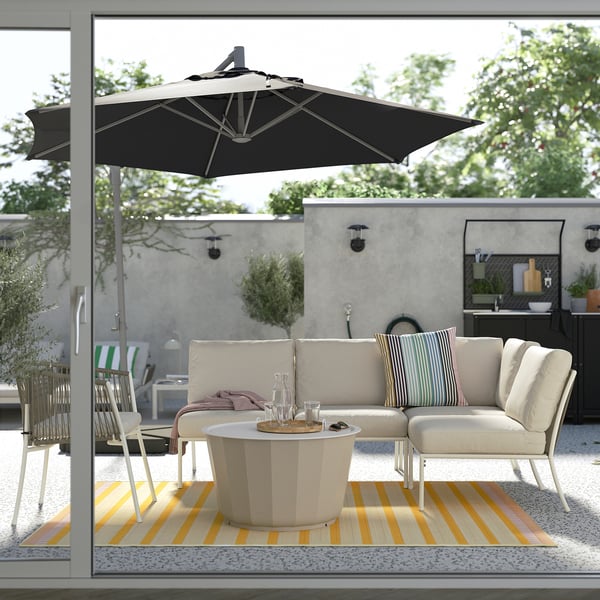 Outdoor patio with a black HISSÖ parasol, white sofa set, and colorful rug over concrete floor.