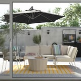 Outdoor patio with a black HISSÖ parasol, white sofa set, and colorful rug over concrete floor.